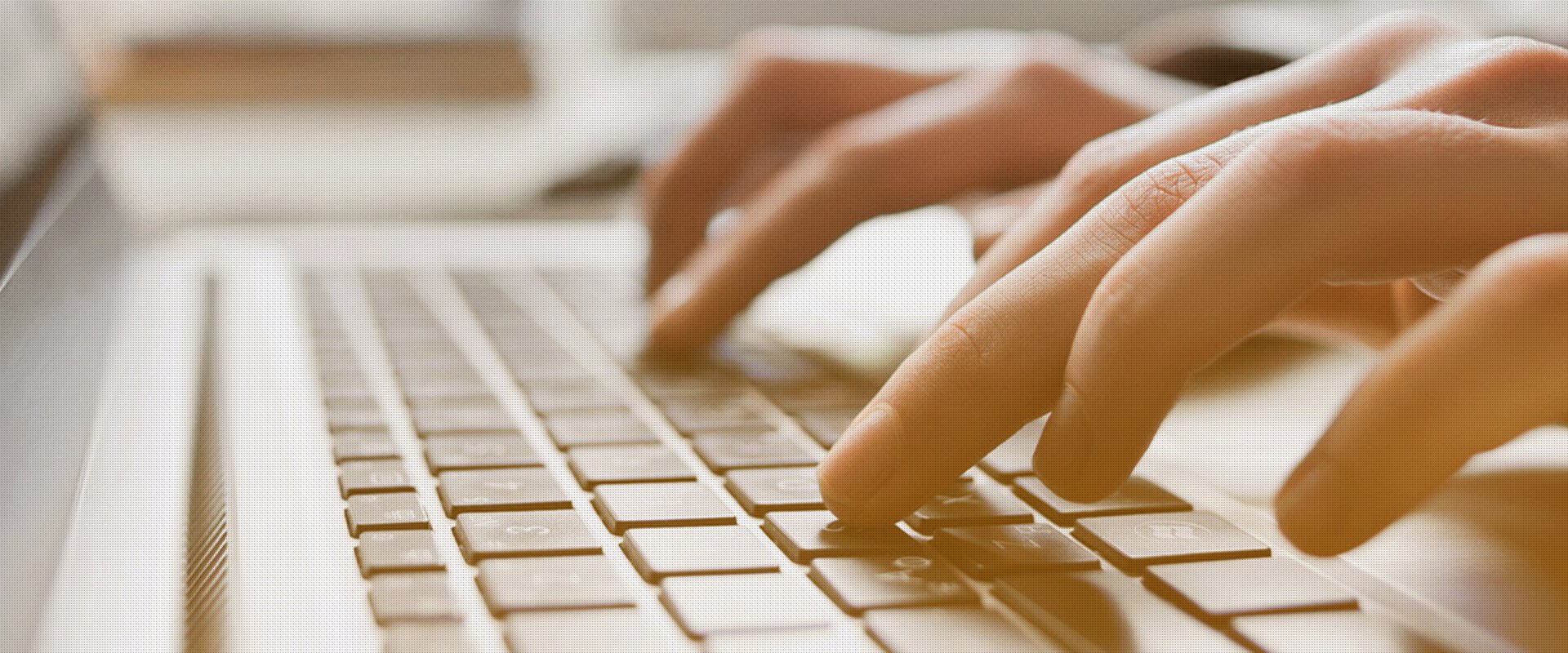 Hände tippen auf einer Laptop-Tastatur, Fokus auf den Fingern mit unscharfem Hintergrund.