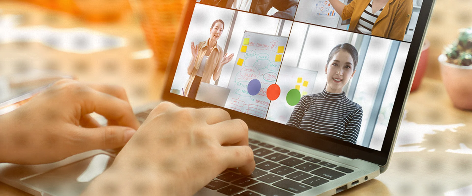 Nahaufnahme von Händen auf der Tastatur eines Laptops während eines virtuellen Meetings mit vier Teilnehmerinnen, die über Video kommunizieren. 